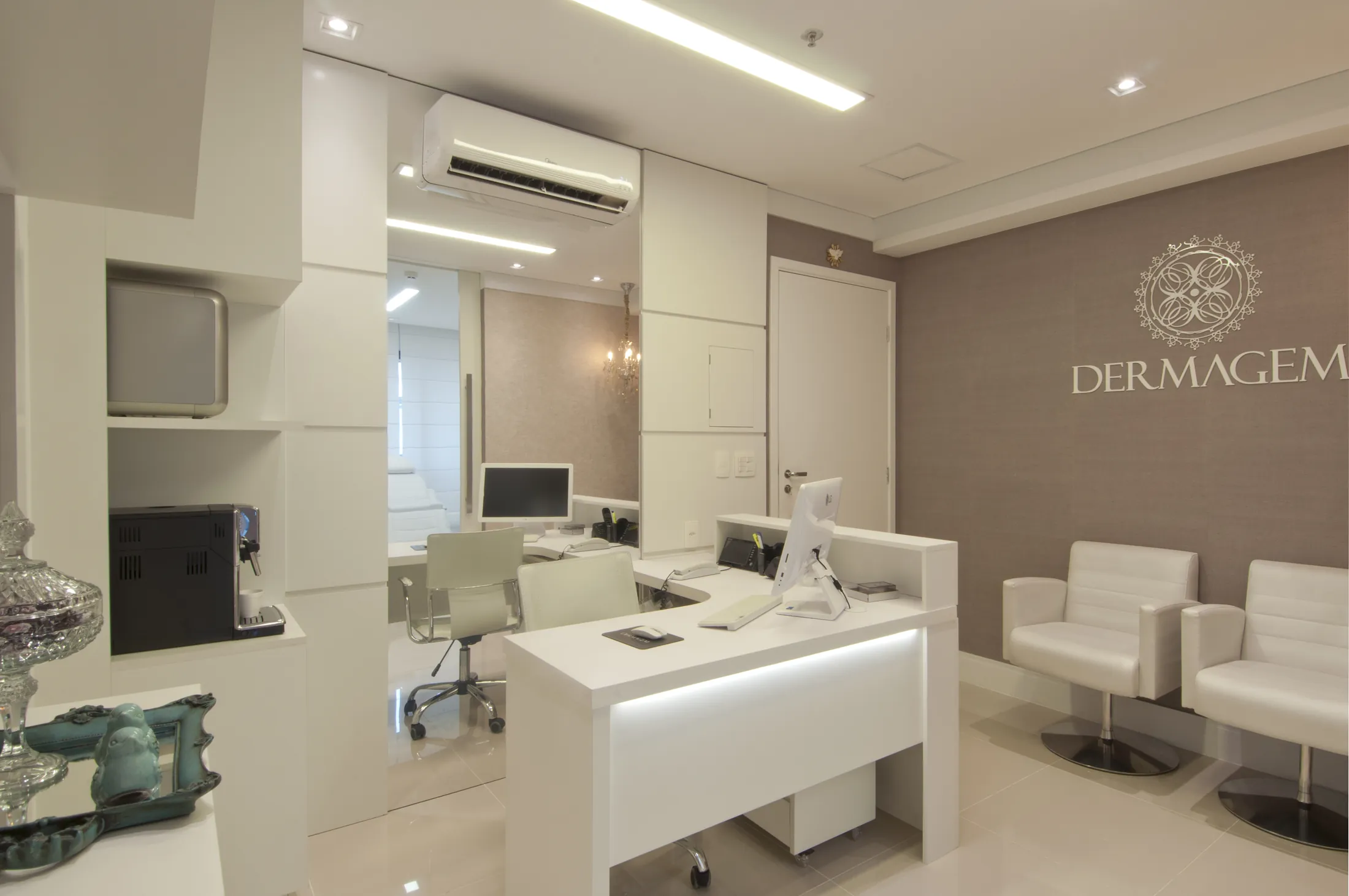 Recepção de clínica com bancada branca, poltronas estofadas e a marca Dermagem em relevo na parede