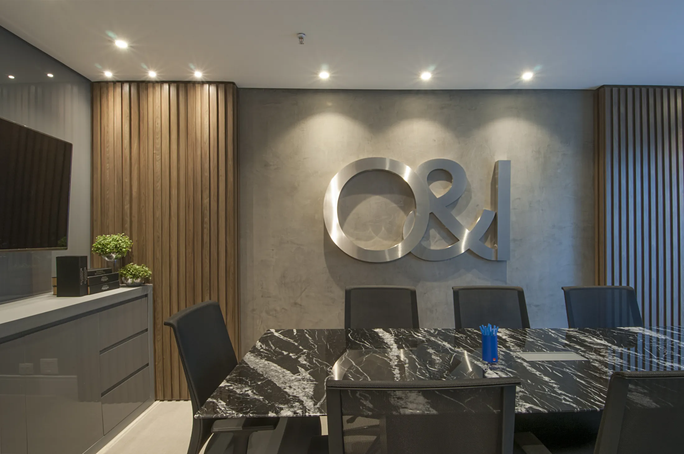 Sala de reunião com mesa de mármore escuro, cadeiras executivas e a marca O&I em metal na parede
